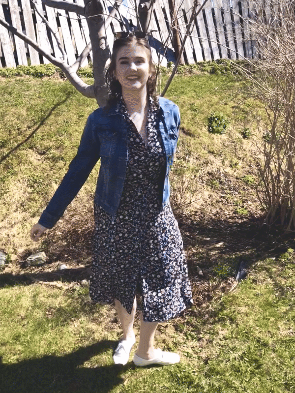 A GIF of Julianne laughing and spinning outside. She wears Ray Ban sunglasses on her head, a navy 90s midi dress, a denim jean jacket, and white leather Keds sneakers.